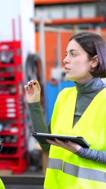 Robot silah fabrikasının üretim hattını kontrol ederken gülümseyen kadın ve erkek mühendisler.