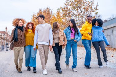 Çok ırklı arkadaşlar gülümsüyor, konuşuyor ve şehir sokaklarında kuyrukta yürüyorlar.