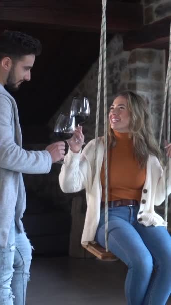 カップルは 自宅の屋根裏にインストールされたスイングにワインをグラスを持っています ロマンチックな夜にカップルのライフスタイル ビデオ — ストック動画