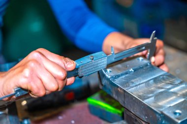 Kesik parmaklı bir operatör, bir CNC makine merkezi aracılığıyla yüksek teknolojili, sayısal kontrol atölyesinde değirmen kesicileri olan bir şirkette çalışıyor. Ölçümleri kalibre ile alıyor