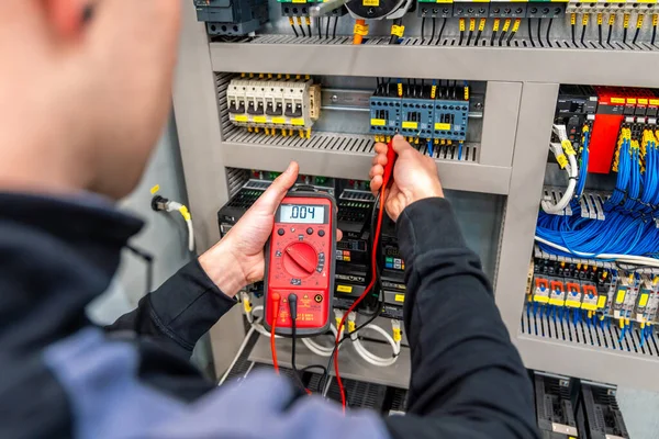 Close-up of a worker measuring and repairing an electrical system panel