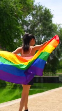 Parkta yürüyen LGBT bayrağıyla beyaz esmer bir kadın. Özgür ve cinsel tercihleriyle gurur duyan lezbiyen bir kadın.