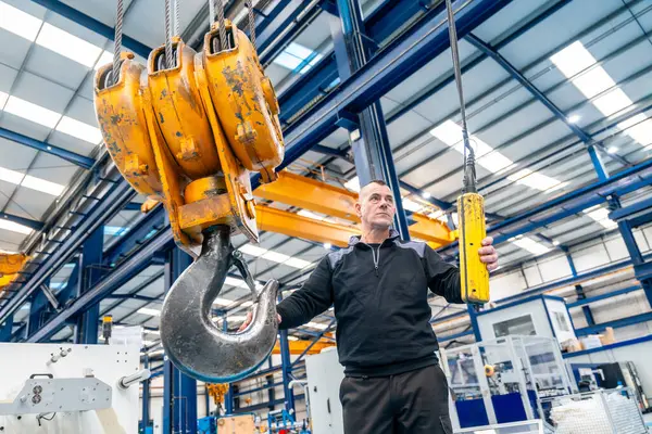 Man commanding the hook of an industrial crane with remote control in a logistics factory