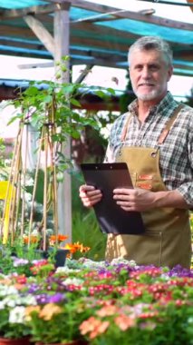 Bahçıvan ya da çiçekçi çiçek serasının içindeki bir çocuk odasında gün batımında bir klasörle envanter çıkarıyor.