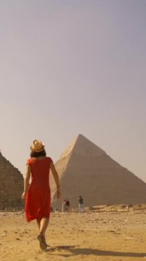 Kırmızı elbiseli ve hasır şapkalı genç bir turistin Giza piramitlerinde yürürken görüntüsü. Kahire, Mısır