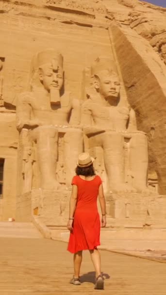 ヌビアのナセル湖の隣にあるヌビアの南エジプトにあるアブ シンベルの寺院の隣にあるネファーリの寺院に向かって歩いている赤いドレスの若い女性 ファラオラムセス2世の神殿 4Kビデオ — ストック動画