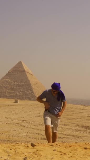 一个身穿蓝色衣服头戴头巾的年轻游客走在吉萨金字塔旁边 埃及开罗 — 图库视频影像