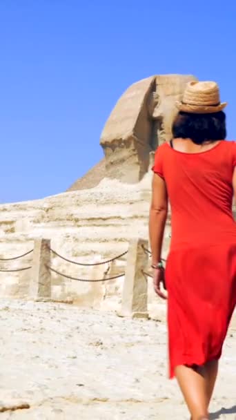 一位身穿红色衣服 头戴草帽的年轻的白人黑发女子正在参观银座金字塔旁边的银座大狮身人面像 埃及开罗 — 图库视频影像
