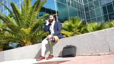 Protez bacaklı mutlu işadamı, mali bir binanın önünde oturan cep telefonuyla konuşuyor.