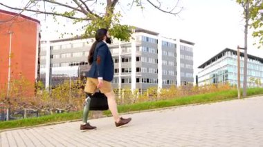 Şehir parkında yürüyen protez bacaklı bir işadamının arka görüntüsü.
