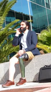 Protez bacaklı mutlu işadamı, mali bir binanın önünde oturan cep telefonuyla konuşuyor.