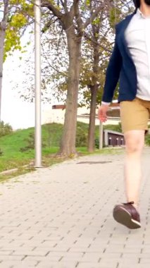 Şehir parkı boyunca dizüstü bilgisayar çantası taşıyan protez bacaklı bir iş adamının ön görüntüsü.