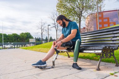 Ampüte atlet, parktaki bankta oturarak yapay koşu bacağını düzeltiyor.