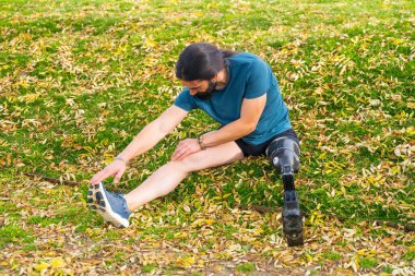 Ampüte olmuş bir sporcunun parkta koşmadan önce esneme hareketi.