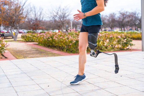 Вид сбоку на нижнюю часть инвалида с протезной ногой, бегущего в городском парке