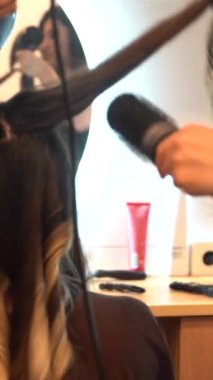 A brunette girl sitting in the beauty salon drying her hair with the dryer, hairdressing