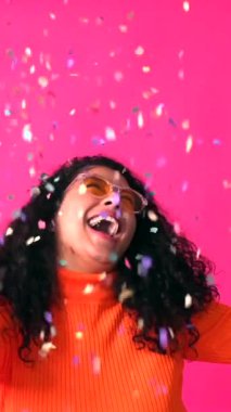 Having fun throwing confetti, Curly-haired woman on a pink background, disco party concept