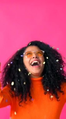 Smiling throwing confetti, Curly-haired woman on a pink background, disco party concept