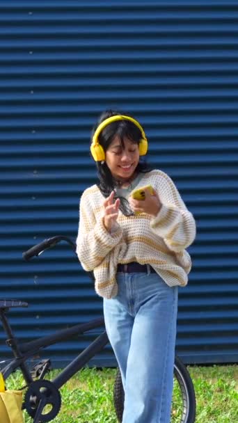 Азійська Дівчина Танцює Слухаючи Музику Жовтими Навушниками Синьому Фоні Коледжу — стокове відео