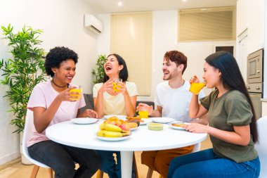 Evde sağlıklı kahvaltı ederken gülen çok ırklı bir arkadaş grubu.