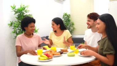 Evde sağlıklı kahvaltı ederken gülen çok ırklı bir arkadaş grubu.