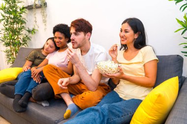 Ev arkadaşları ilginç bir film izliyorlar kanepede birlikte oturup dikkat ediyorlar ve patlamış mısır yiyorlar.