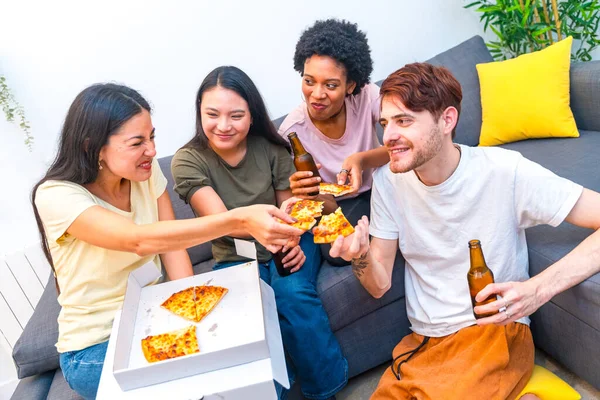 Happy friends sharing a pizza and drinking beers together at home sitting on the sofa