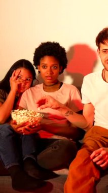 Bir terör filmi gecesinde çok ırklı arkadaşlar kanepede oturup patlamış mısır yiyor ve yüzleri kapatıyorlar.
