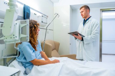 Doktor hastane yatağında bir hastayı ziyaret ediyor ve onunla konuşuyor.