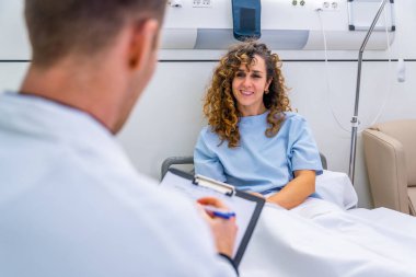 Hastane yatağında kadın hastayla ilgilenen tanınmayan bir doktorun arka görüntüsü.