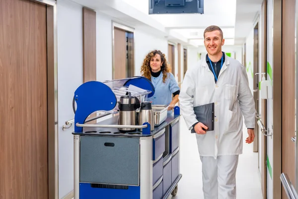 Doctor next to a nurse with a trolley with coffee in the corridor of an hospital