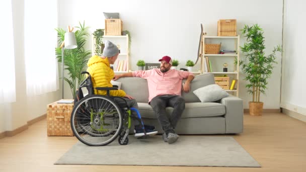 自宅でソファーに座っている間 車椅子で障害のある友人をサポートする男 — ストック動画