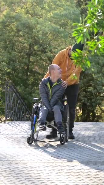 Cuidador Empurrando Cadeira Rodas Homem Com Deficiência Sorridente Parque Urbano — Vídeo de Stock