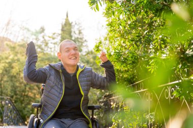 Tekerlekli sandalyedeki engelli adam parkta hayatın ve doğanın tadını çıkarıyor.