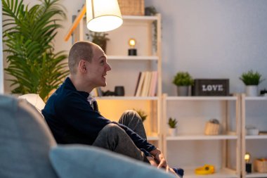 Geceleri kanepede tek başına oturan üzgün, engelli bir adamın yan görüntüsü.