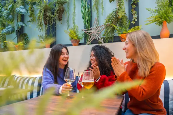 Three female friends smiling while applauding a celebrating with wine in a cafeteria