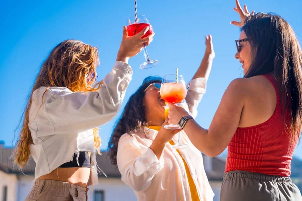 Three women dancing and drinking alcohol at the roof party in summer