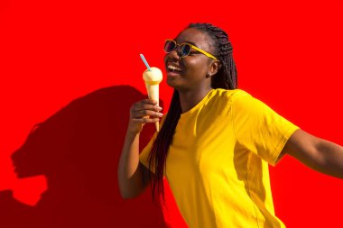 Kırmızı arka planda, yazın dondurma yiyen Afrikalı genç bir kadının portresi.