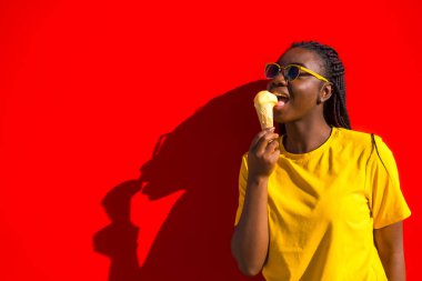 Yazın kırmızı duvarın yanında dondurma külahını yalayan Afrikalı bir kadın.