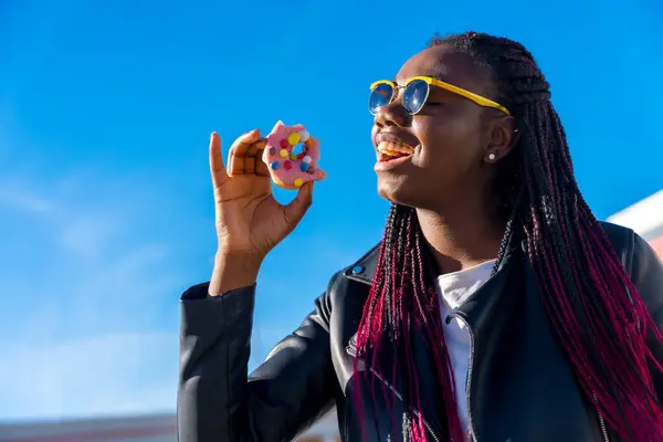 Happy african woman enjoying eating a doughnut in a sunny day outdoors