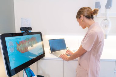 Modern diş kliniğinde bir dişçi, müşterisinin monitöründeki 3D röntgene bakıyor.