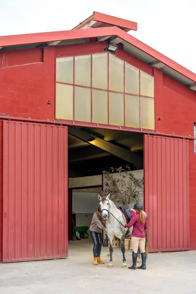 Wide view of an outside building with a female jockey about to ride a horse in equestrian center