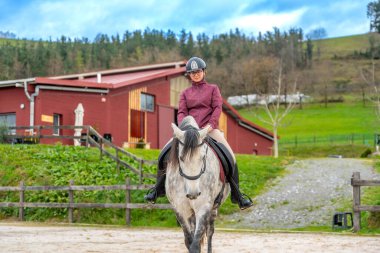 Sakin bir binicilik merkezinde beyaz bir ata binen genç bir kadının ön görüntüsü.