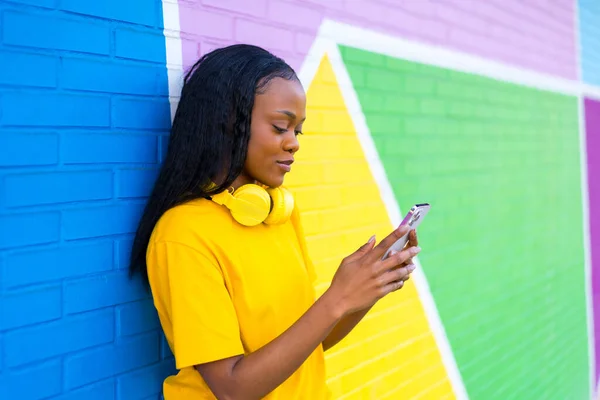 Side view portrait of a beauty african young woman using phone leaning on a colorful wall