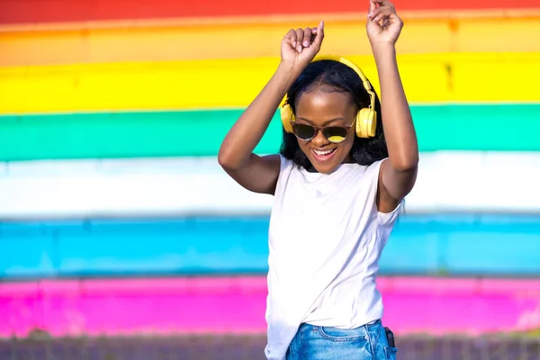 Happy and joyful african woman with headphones dancing in an urban park
