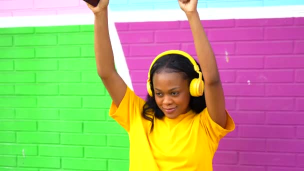 性感的非洲女人一边跳舞一边看着摄像机 一边在五彩缤纷的墙壁上听音乐 — 图库视频影像