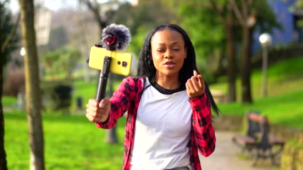 若いアフリカ人女性が市内の都市公園で携帯電話でビデオを録画 — ストック動画
