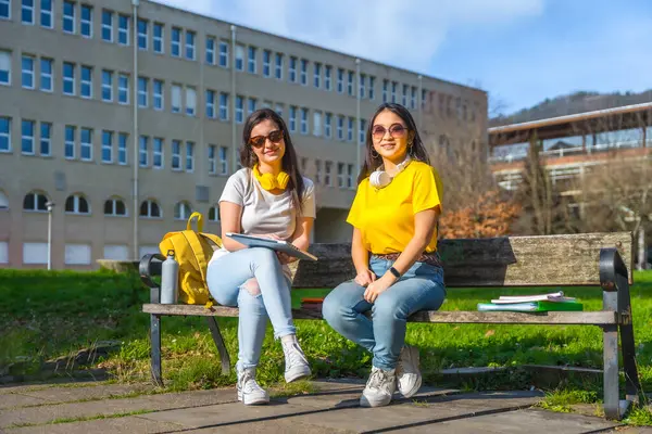 Portrait of two university friends sitting on a bench in the campus
