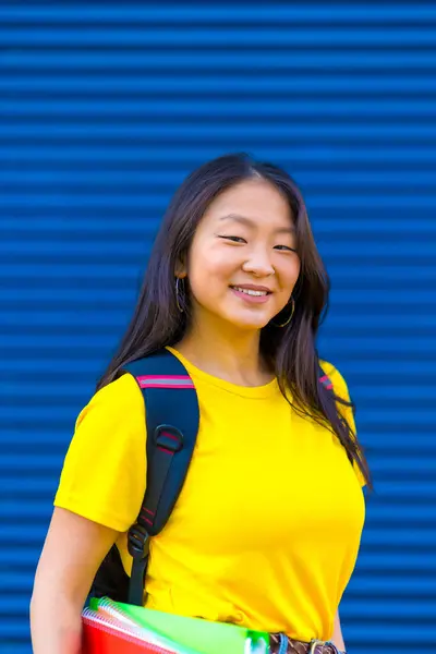 Vertical photo of a chinese international student smiling at camera in a blue background