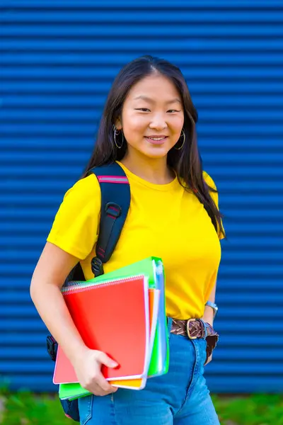 Vertical photo of a chinese student holding textbooks smiling at camera